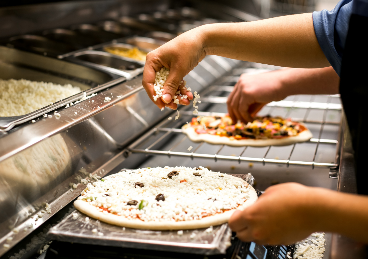 Pizza being topped with hand dropping vegetables onto pizza