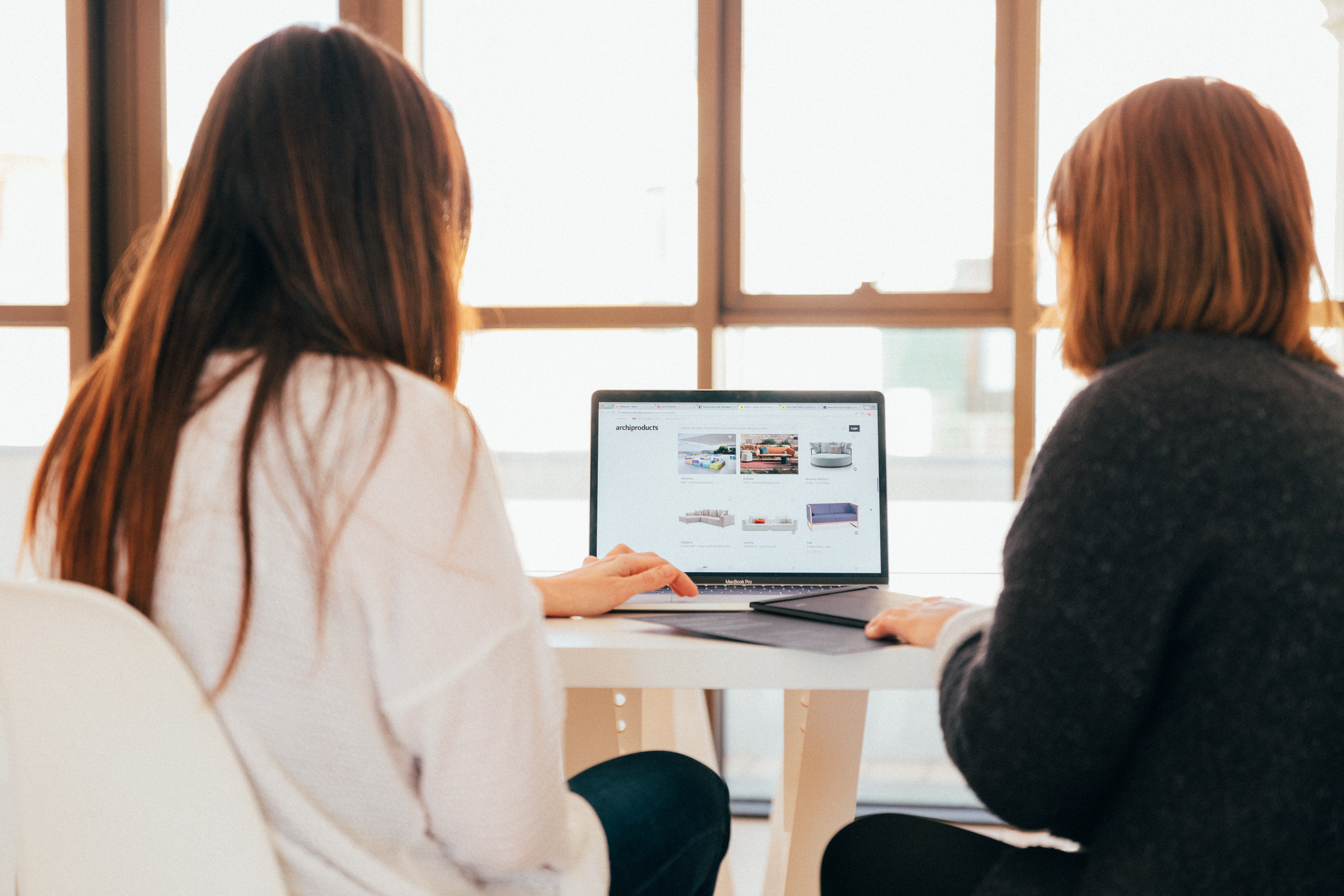In an office, looking over the shoulder of two females looking at laptop computer