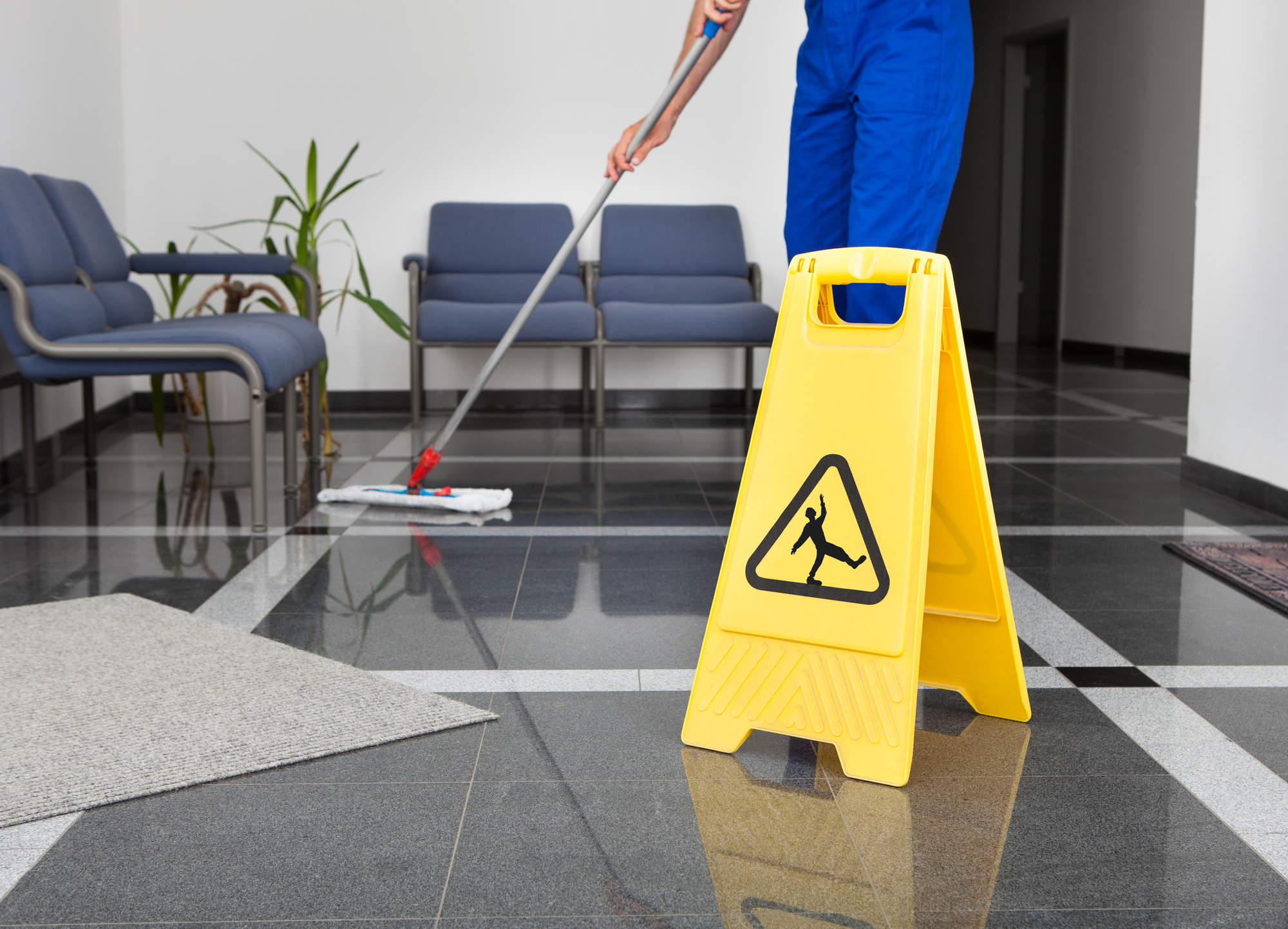yellow caution wet floor sign with bottom half of man mopping the floor in the background
